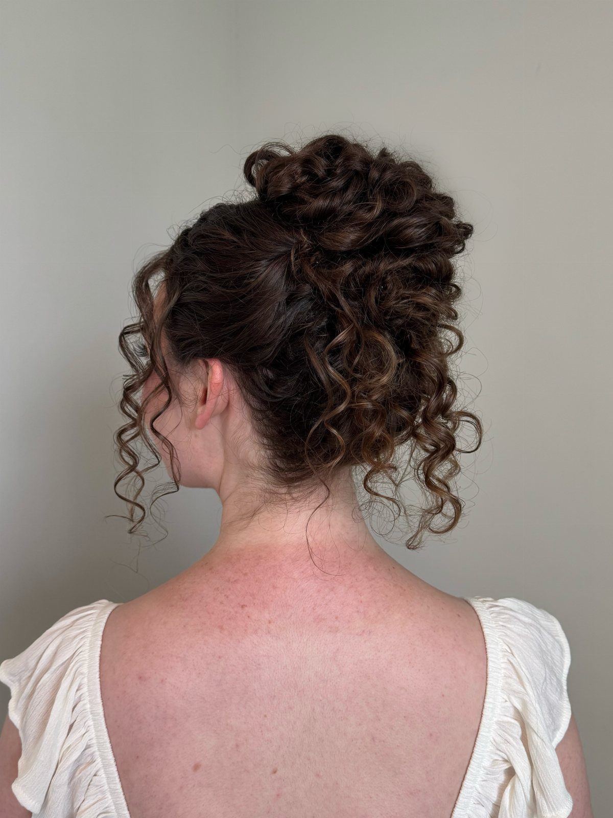 Curly brown hair styled in a high voluminous updo with loose tendrils.