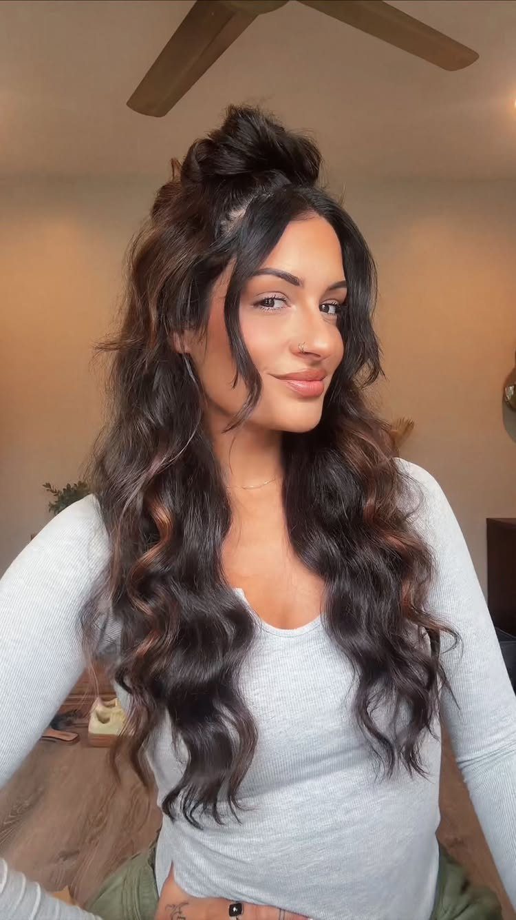 Woman with wavy brown hair styled in a half-up topknot and loose curls.