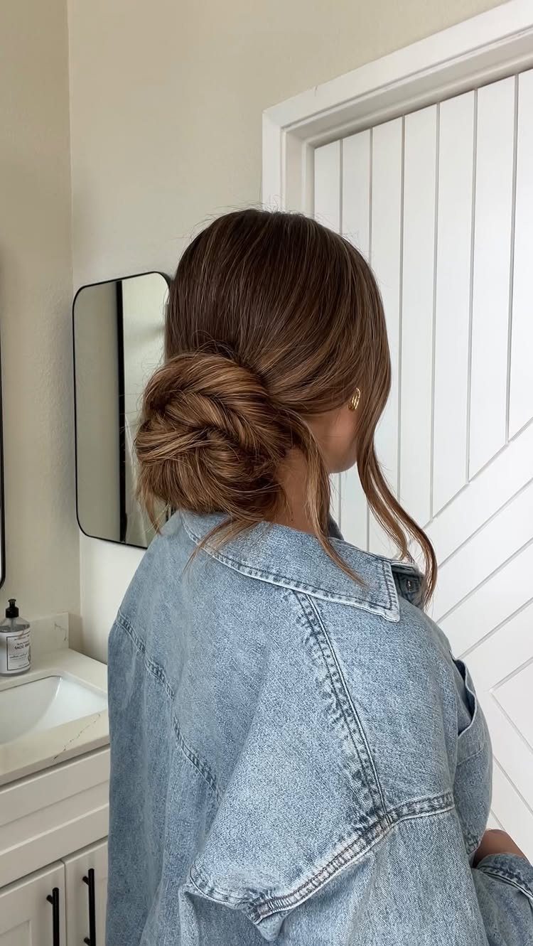 Woman with brown hair styled in a casual low bun wearing a denim jacket.