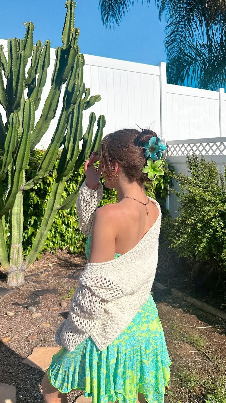 Woman with a floral bun hairstyle wearing a green dress and white crochet cardigan.