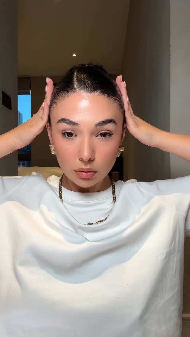 Woman with a slicked back bun and center part wearing a white t-shirt.