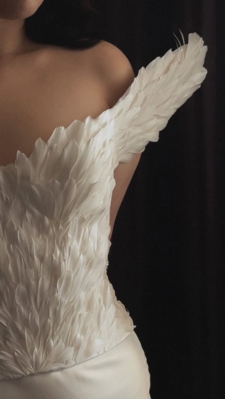 14 White Feather Gown Ideas, From Bridal Capes to Tea-Length 14 White feather gown bodice with layered plumes on a person against dark background