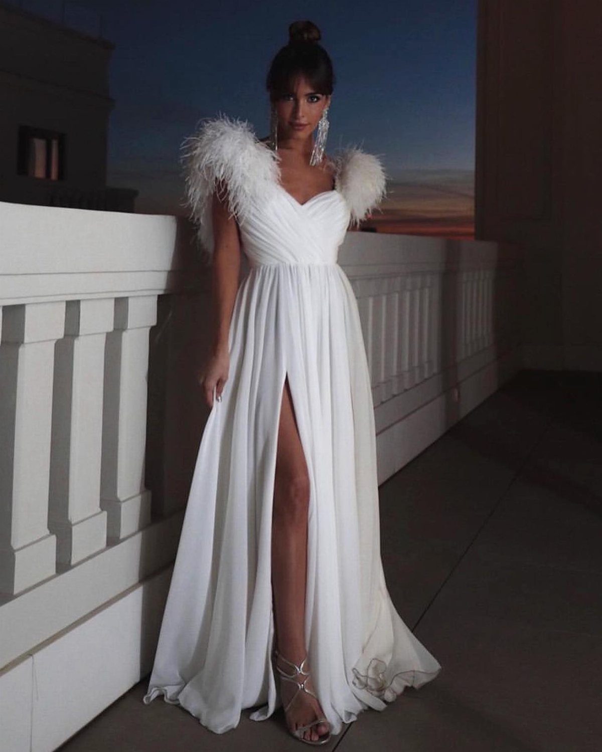 14 White Feather Gown Ideas, From Bridal Capes to Tea-Length 13 Woman in a white gown with feather shoulders and a high leg slit.