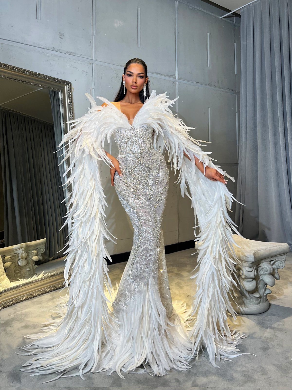 14 White Feather Gown Ideas, From Bridal Capes to Tea-Length 3 Woman in a white sequined mermaid gown with dramatic oversized feather sleeves and hem.