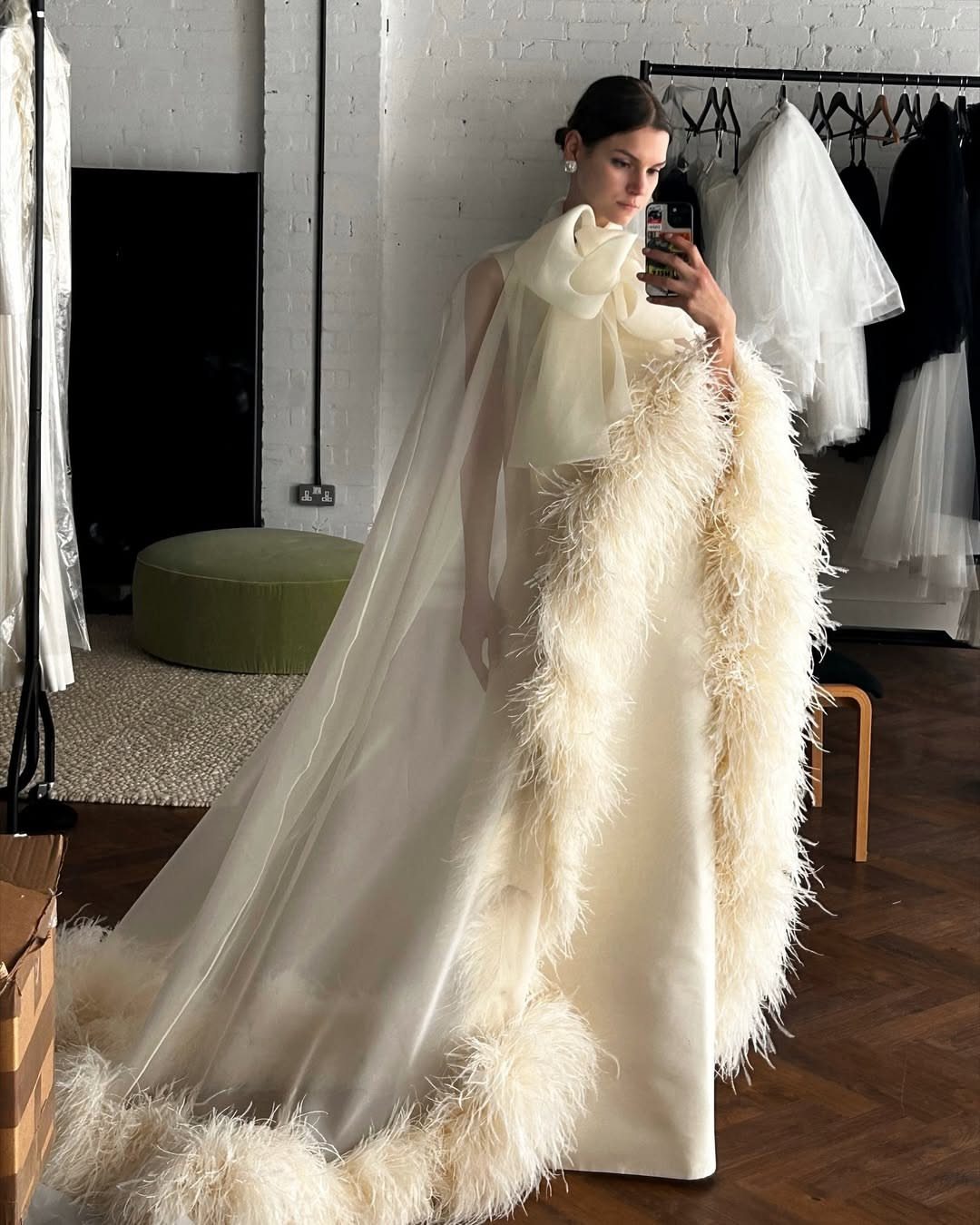 14 White Feather Gown Ideas, From Bridal Capes to Tea-Length 2 Woman wearing a white bridal gown with a sheer feather-trimmed cape and large bow.