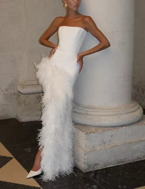 14 White Feather Gown Ideas, From Bridal Capes to Tea-Length 4 Woman in a strapless white column gown with a vertical front feather panel.