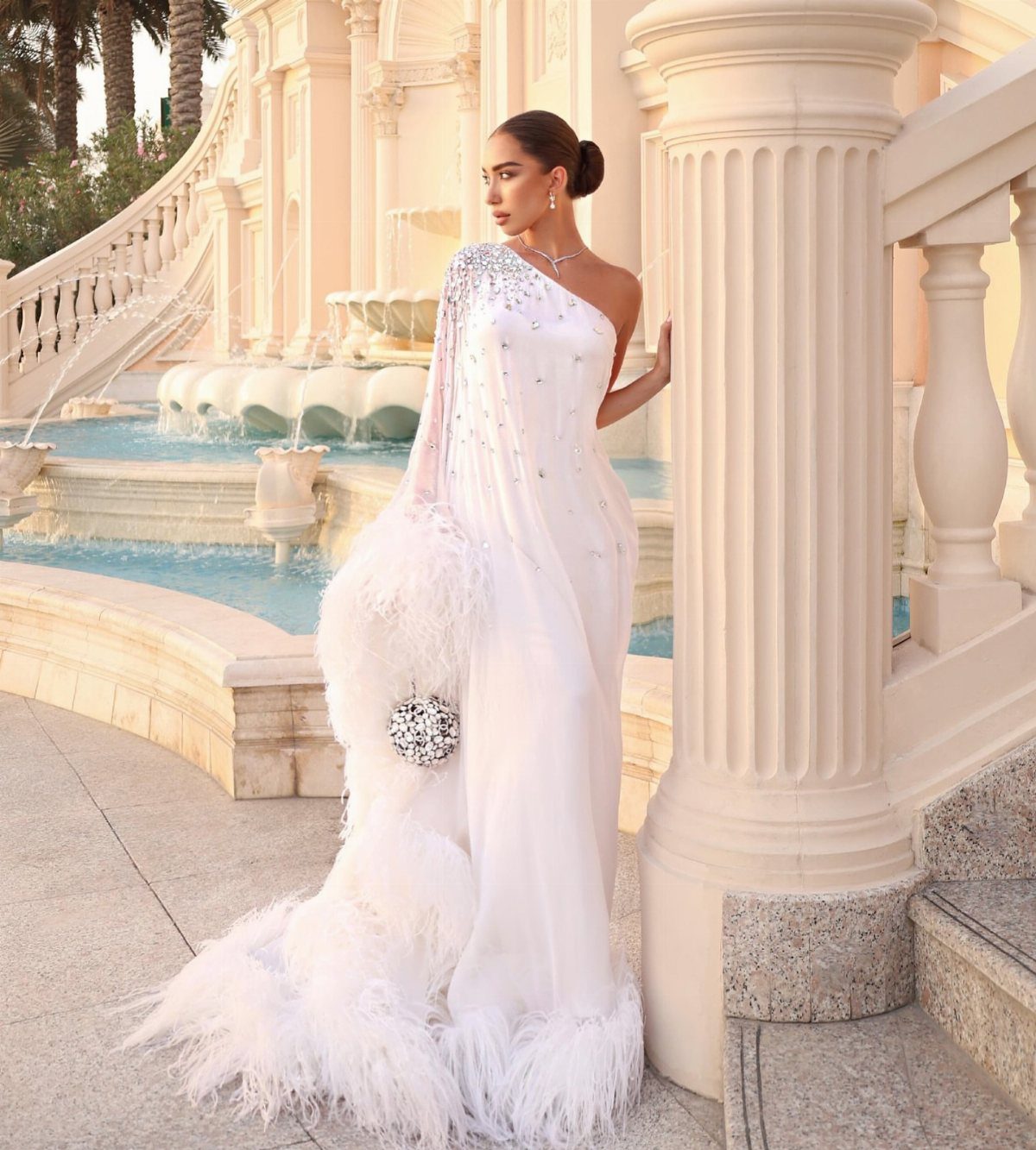 14 White Feather Gown Ideas, From Bridal Capes to Tea-Length 12 Woman in a white one-shoulder gown with sparkling details and white feather trim.