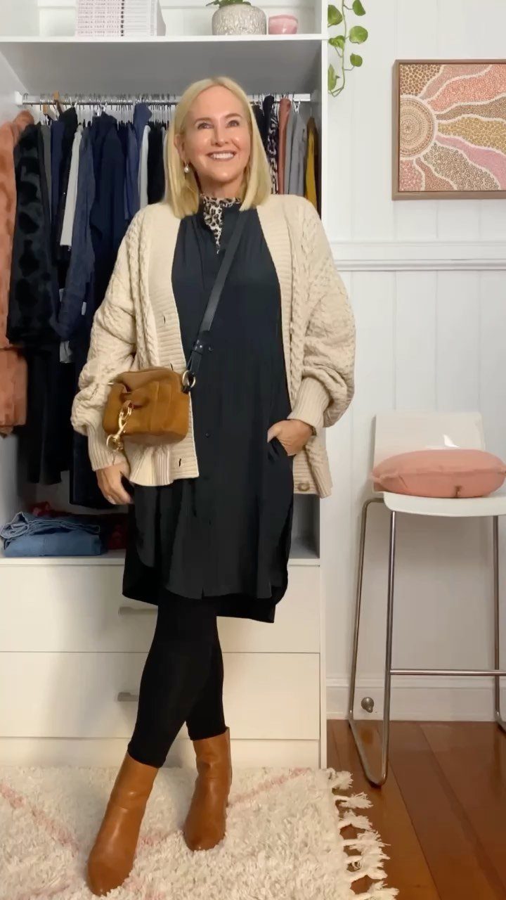 Woman wearing a navy blue dress with a cream cardigan and brown boots.