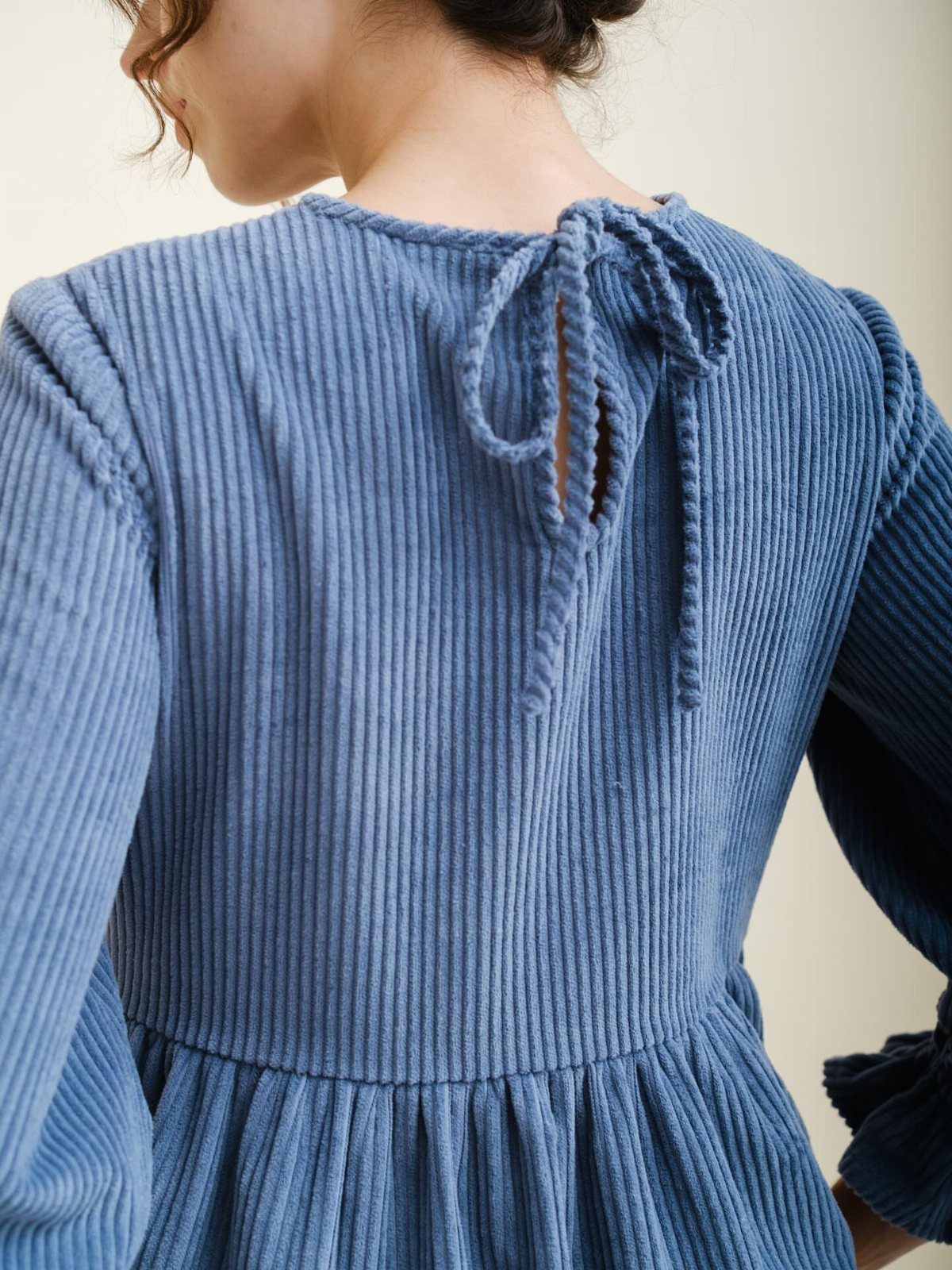 Blue corduroy dress with long sleeves and a tie-back detail on the neckline.