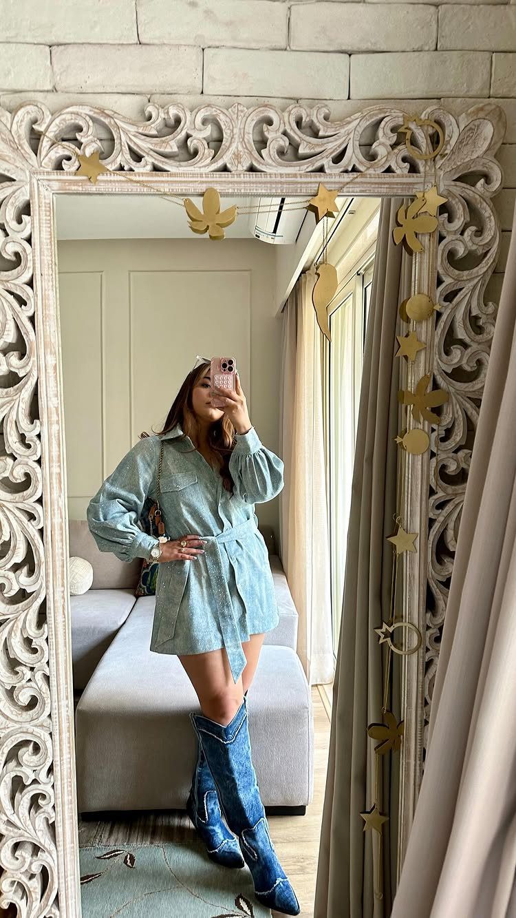 Woman in a light blue denim shirt dress and tall blue boots.