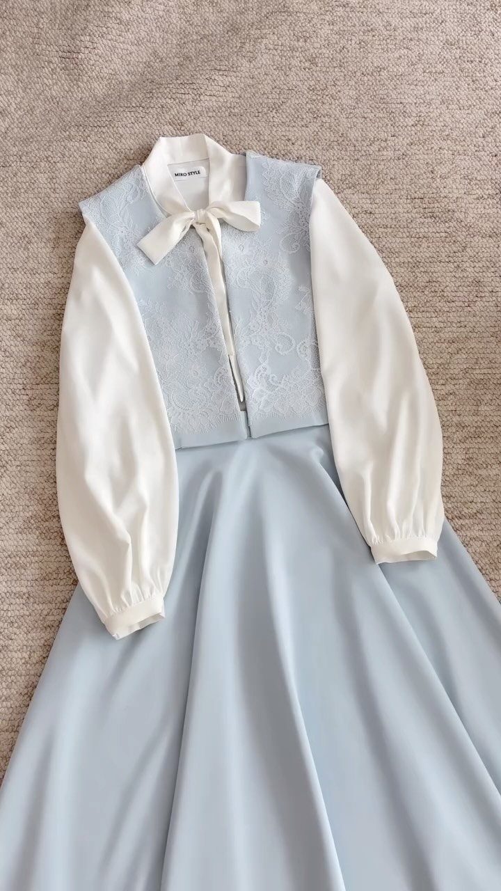 Light blue dress with white long sleeves and a bow on grey fabric
