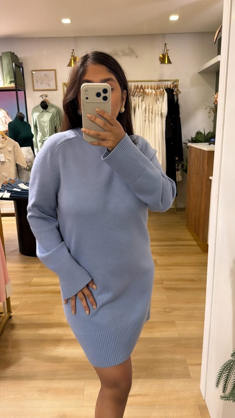 Woman wearing a light blue long-sleeved knit sweater dress in a clothing store.