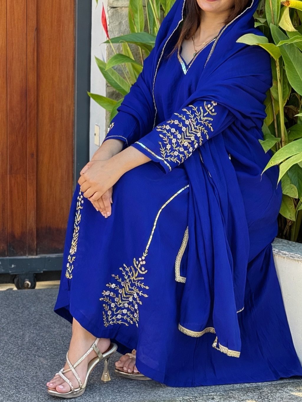 Person in royal blue traditional dress with gold embroidery and gold strappy heels.