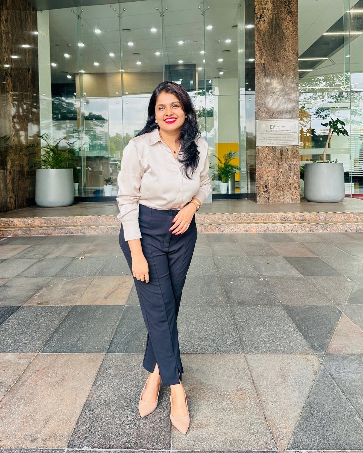 Women Outfit Work Office: 17 Ideas to Refresh Your Look 9 Woman wearing a beige blouse and navy trousers standing before a modern office building.