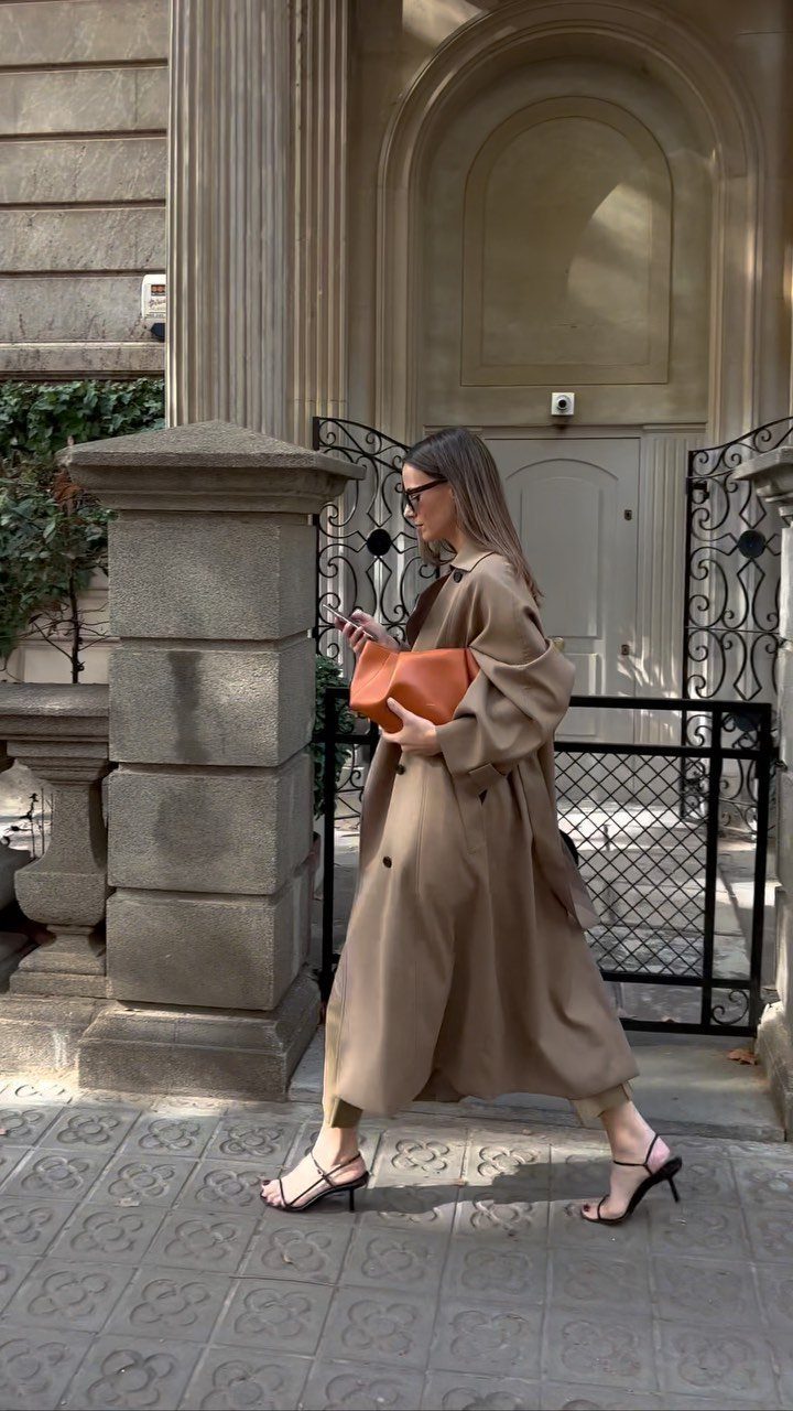 Women Outfit Work Office: 17 Ideas to Refresh Your Look 4 Woman in a long tan trench coat and orange clutch walking on city sidewalk