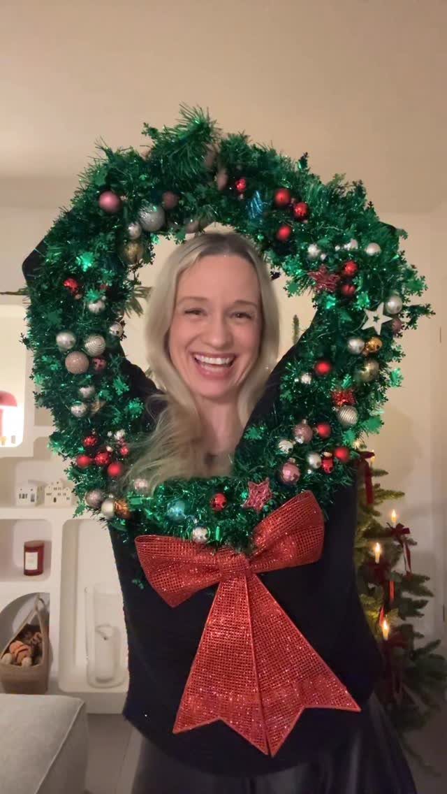 Woman wearing a black ugly Christmas sweater with a large 3D tinsel wreath.