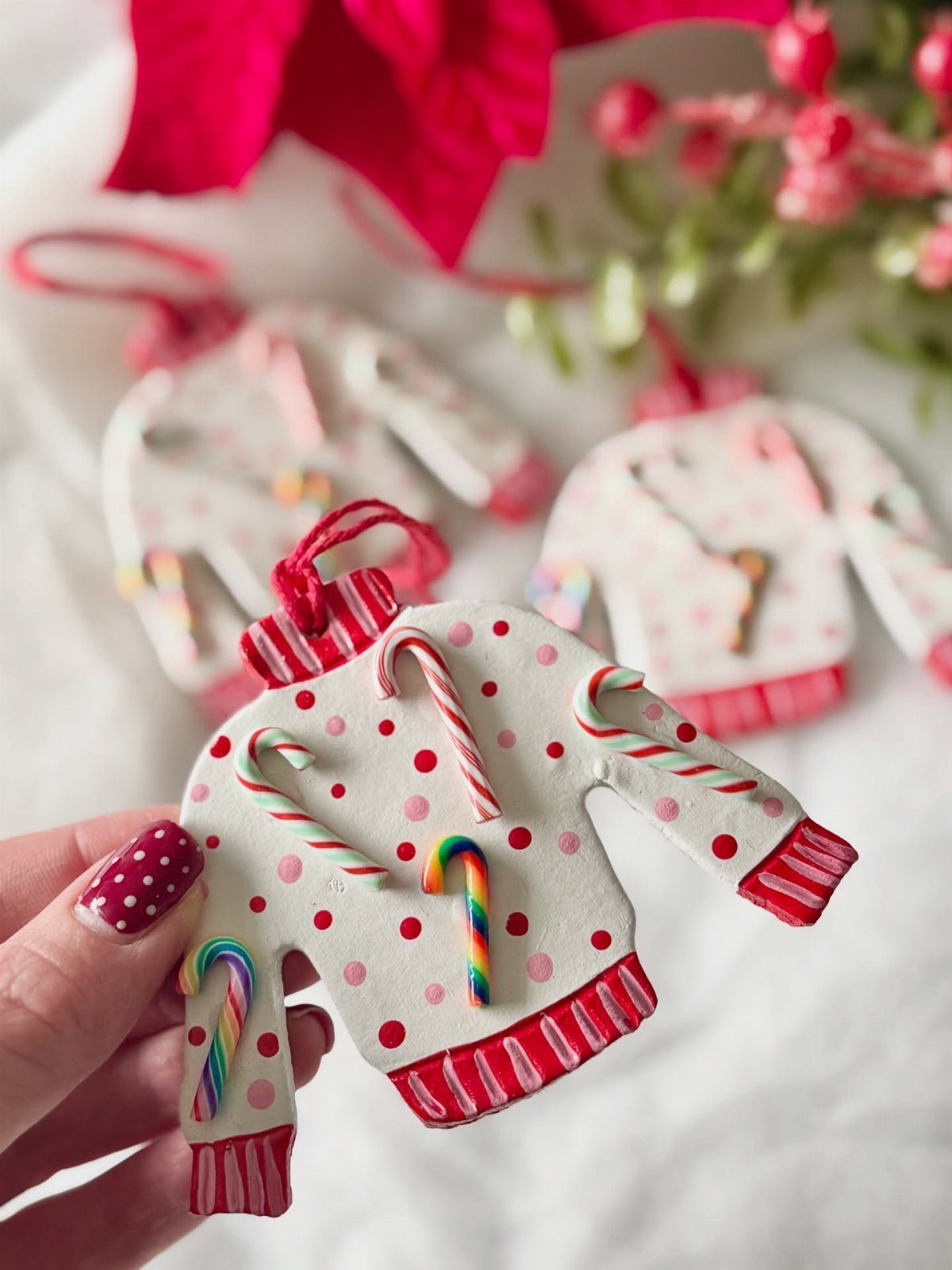 Sweater-shaped ornaments decorated with candy canes and red dots held by a hand.